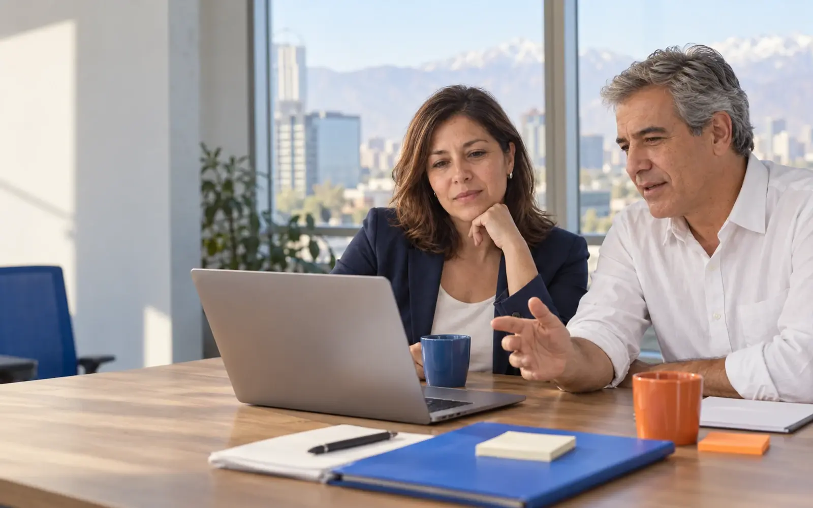 Dos personas revisan una laptop junto a una ventana de oficina.